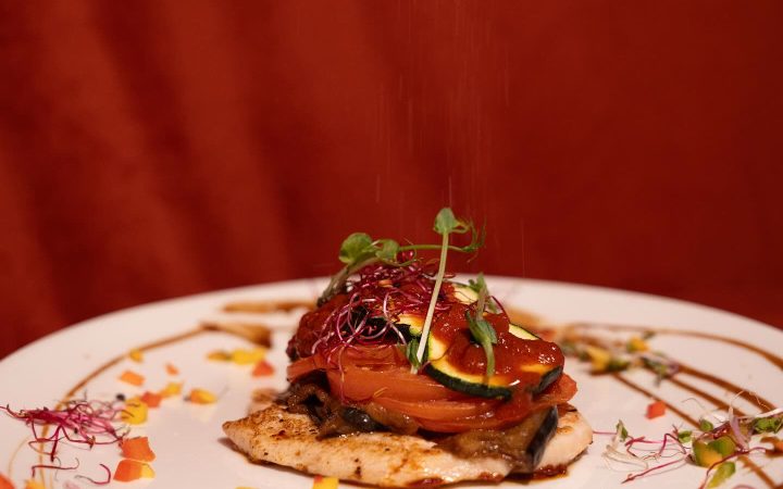 Une pièce de viande grillée garnie de légumes et de micro-pousses sur une assiette décorée