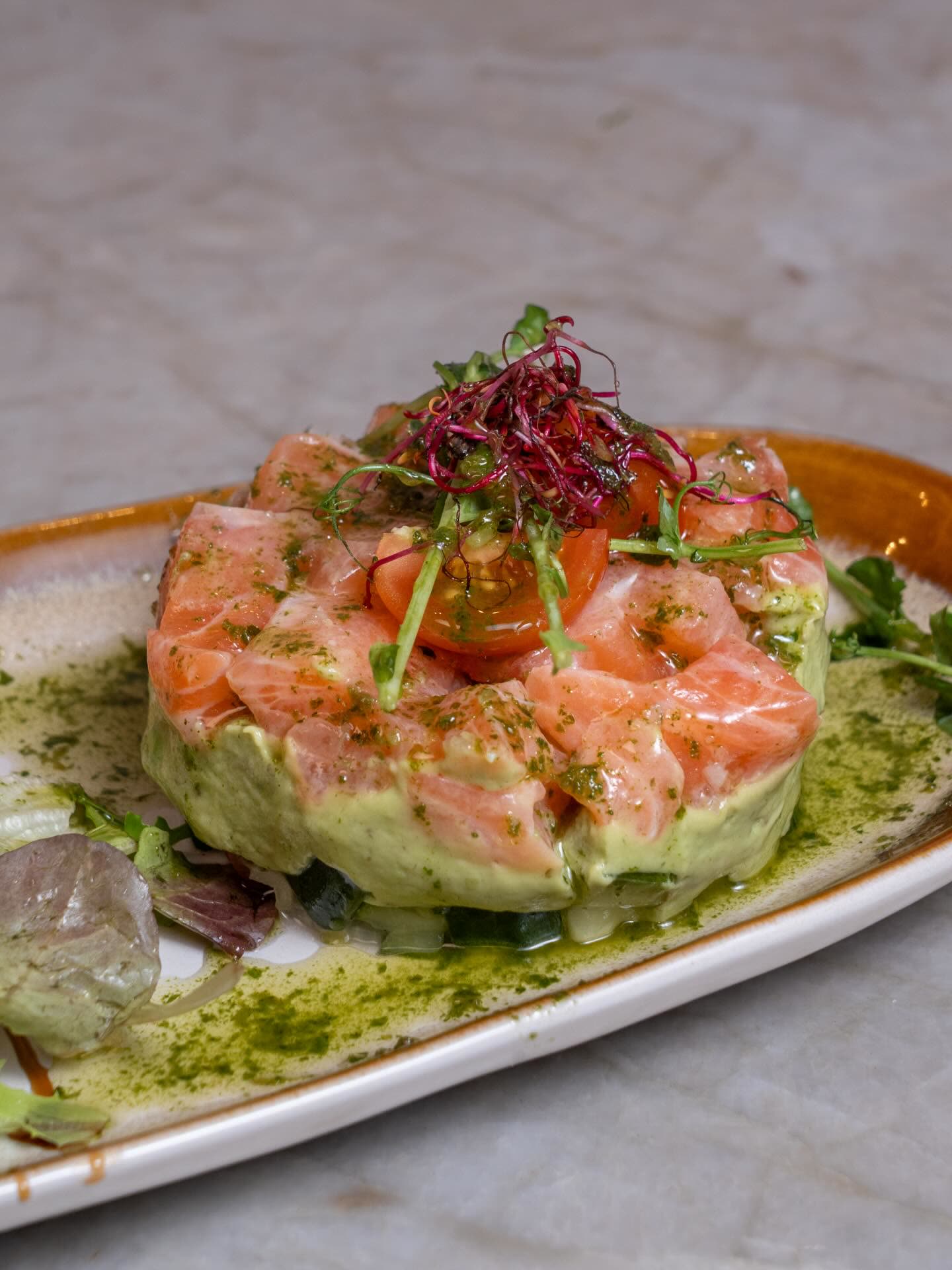 Un tartare de saumon sur un lit d'avocat avec des micro-pousses et des tomates cerises