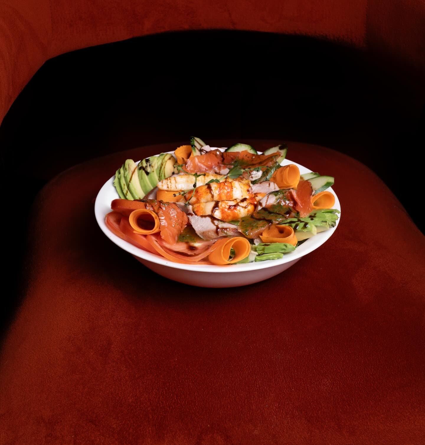 Une salade composée de poisson, crevettes et avocat servie dans une assiette blanche sur un fond sombre